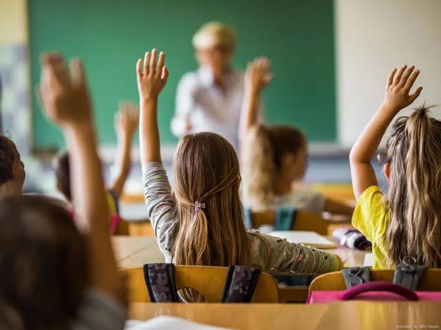 Crianças com as mãos levantadas em uma sala de aula