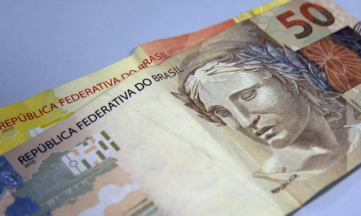 Notas de dinheiro em uma superfície branca representando o pagamento do Bolsa Família