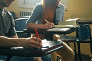 Estudantes em sala de aula escrevendo e fazendo anotações durante a aula.